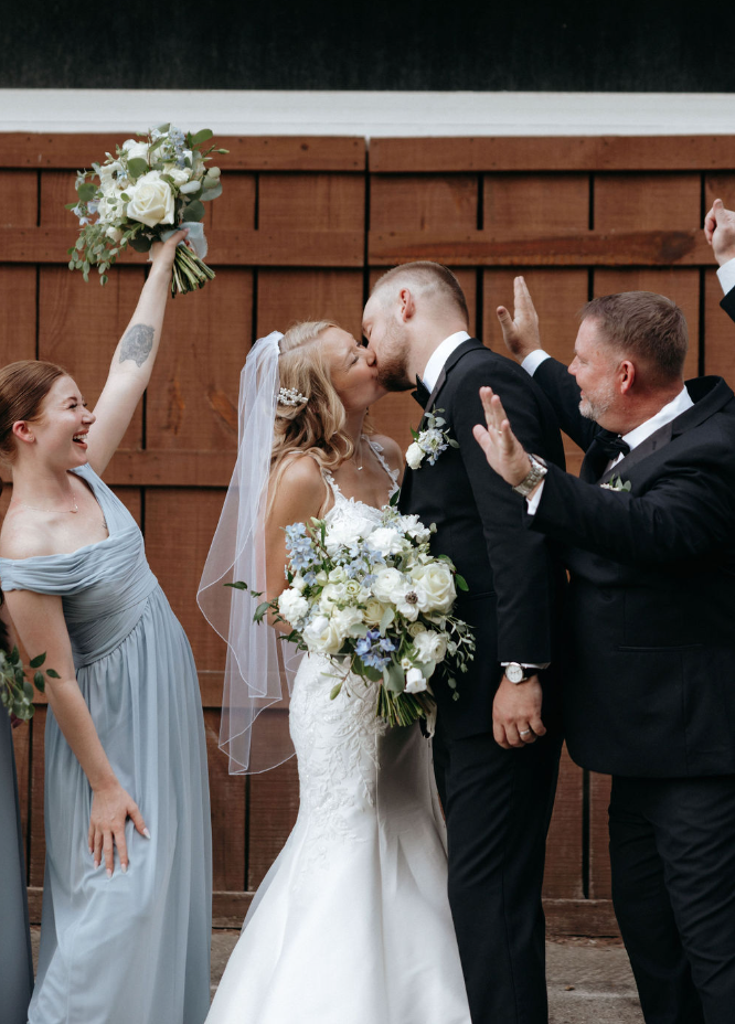 Couple kissing with wedding party cheering